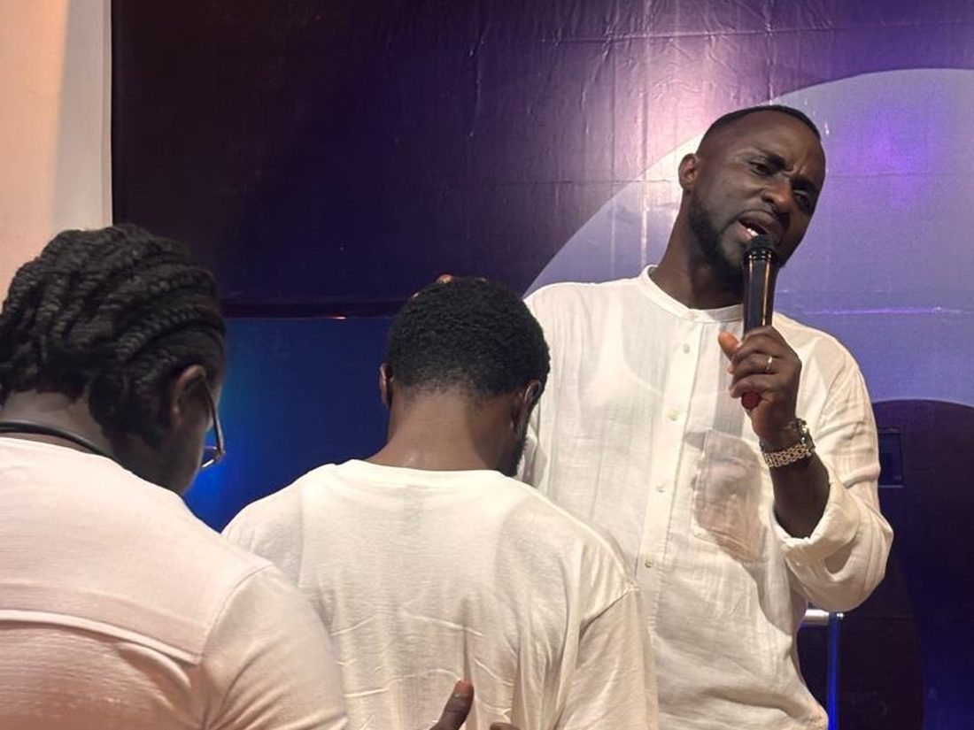 Rev. Fred A. Boateng praying with two young men at the front of the church